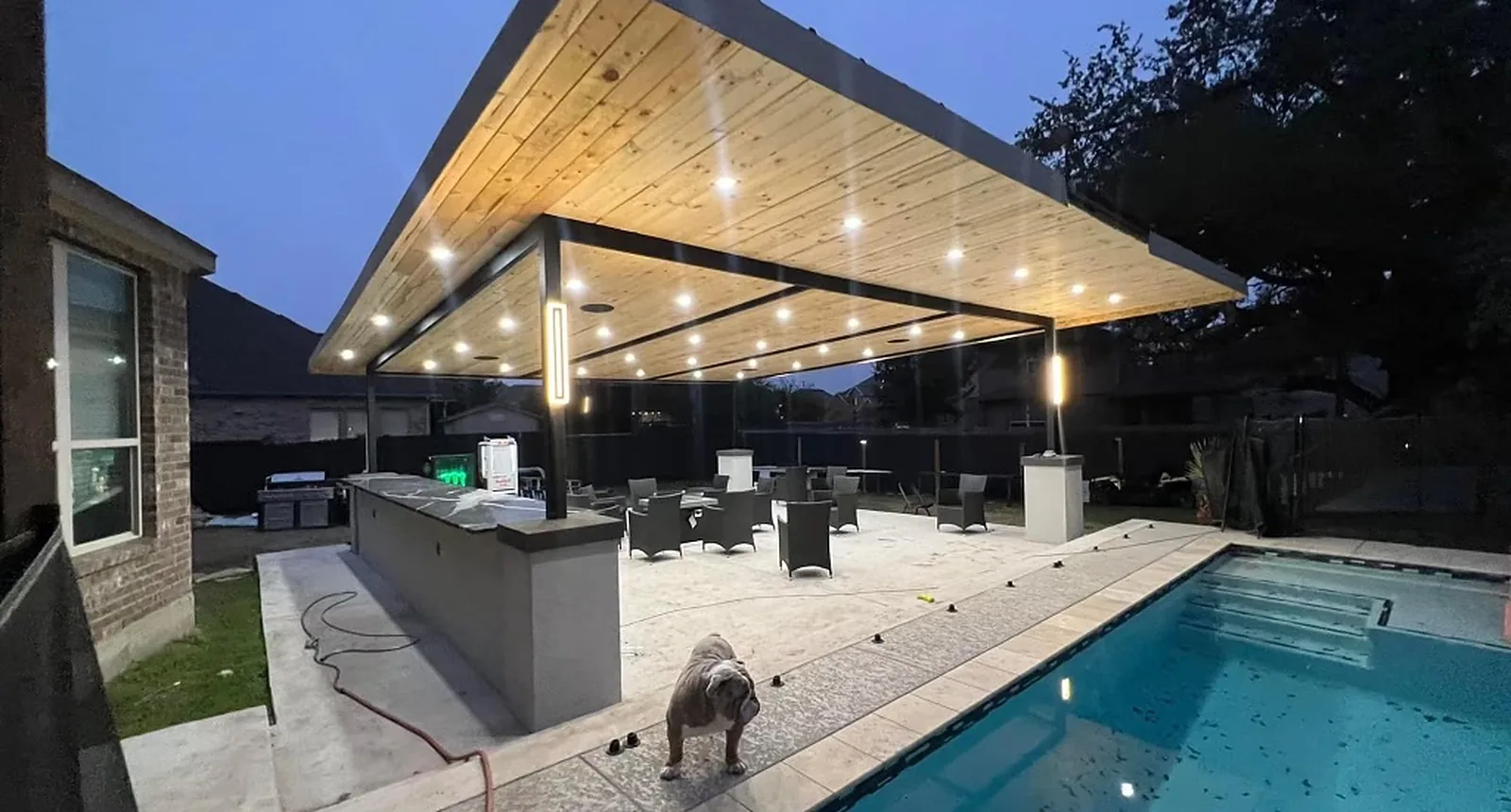 Covered patio with outdoor kitchen and pool lighting at dusk in San Antonio